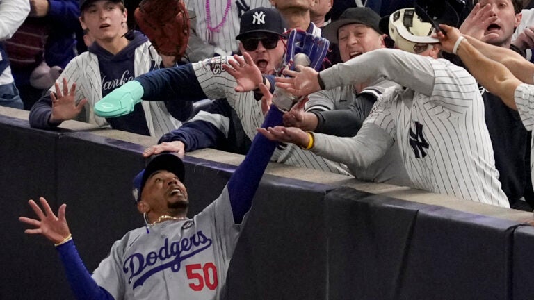 Fans interfere with a foul ball caught by Los Angeles Dodgers right fielder Mookie Betts during the first inning in Game 4 of the baseball World Series against the New York Yankees, Tuesday, Oct. 29, 2024, in New York.
