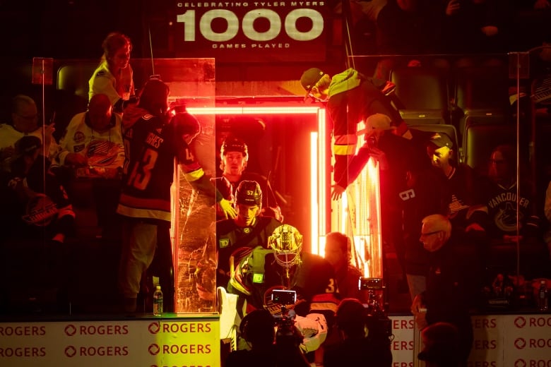 A group of hockey players enter the ice surrounded by fans and red lighting.