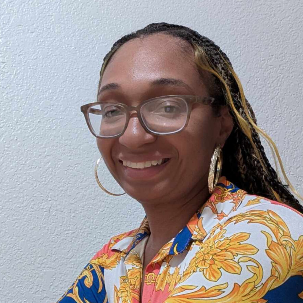 Photo of Jessica 'Nooni' Noble, Editor-in-Chief of Sports and More Sports, smiling warmly while wearing glasses and a vibrant floral-patterned shirt against a neutral background. Image is featured on the webpage, "About Sports And More Sports."