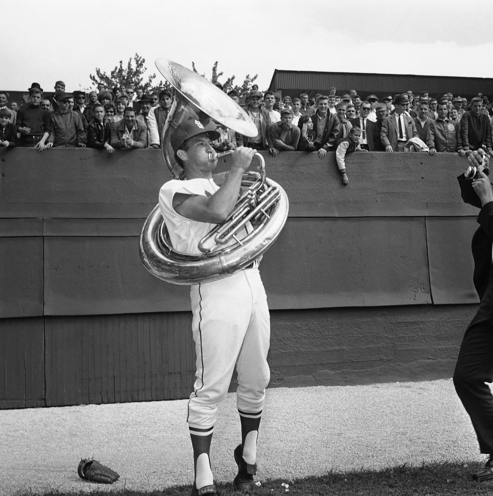 Bob Uecker, during his time as St. Louis Cardinals catcher, clowns around during a workout by playing tuba near the bleachers at Busch Stadium before the start of Game 2 of the 1964 World Series. (AP Photo)