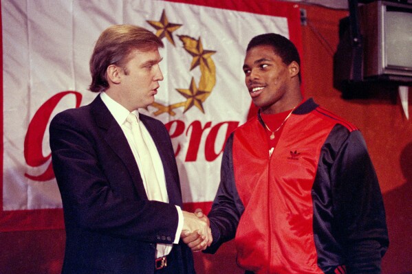 Donald Trump shakes hands with Herschel Walker in New York after agreement on a 4-year contract with the New Jersey Generals USFL football team, March 8, 1984. (AP Photo/Dave Pickoff, File)