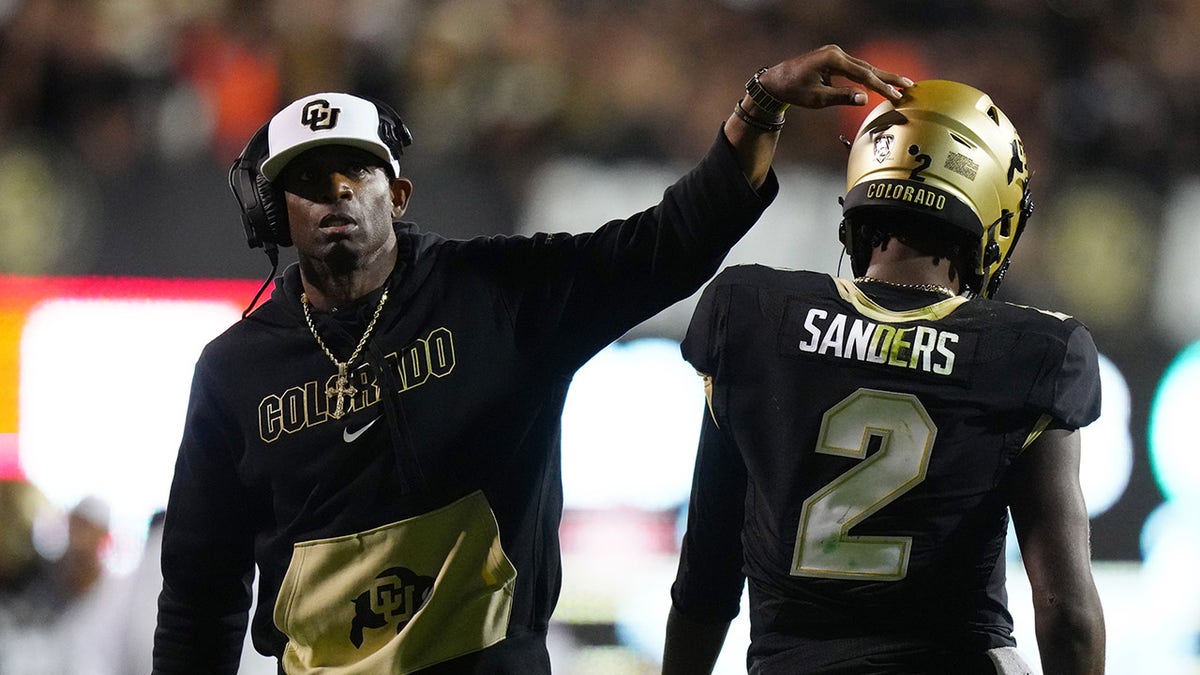 Deion Sanders touching Shedeur Sanders helmet on the football field 