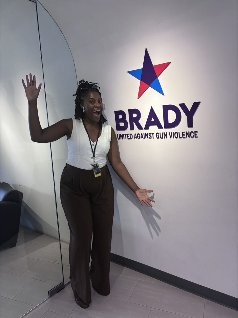 Bri Tollie poses in front a poster for an organization against gun violence.